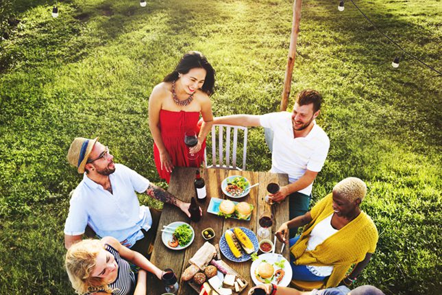 A group of friends having an outdoor meal together on their lawn.